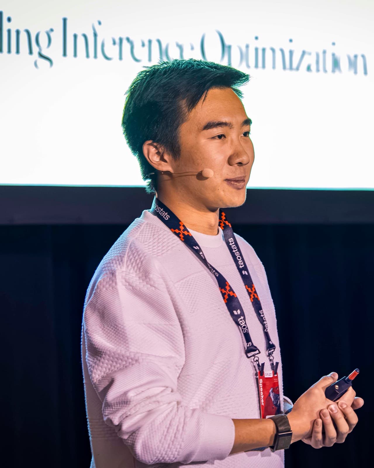 Xavier Lyu holding a clicker on stage, wearing a speaker lanyard